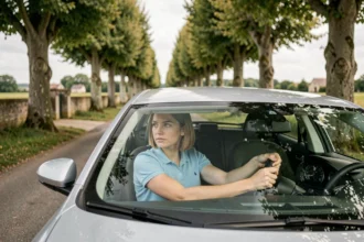 Jeune conductrice dans une voiture d'auto-école sur une route de la Sarthe, vue de l'extérieur à travers la vitre passager